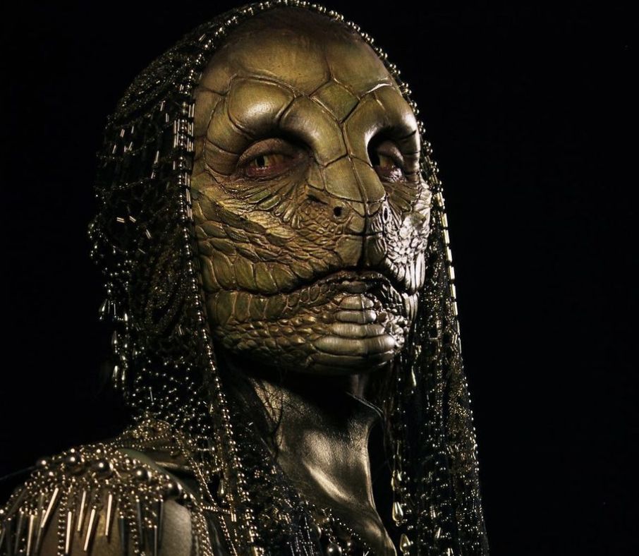 The Crocodile Lady wearing a dark beaded headdress and metallic reptilian mask